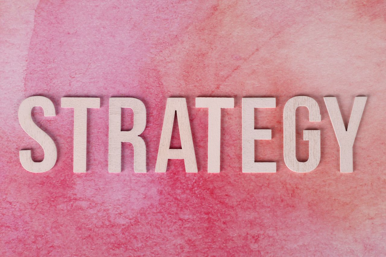 Wooden letters arranged to spell Strategy against a pink textured backdrop.